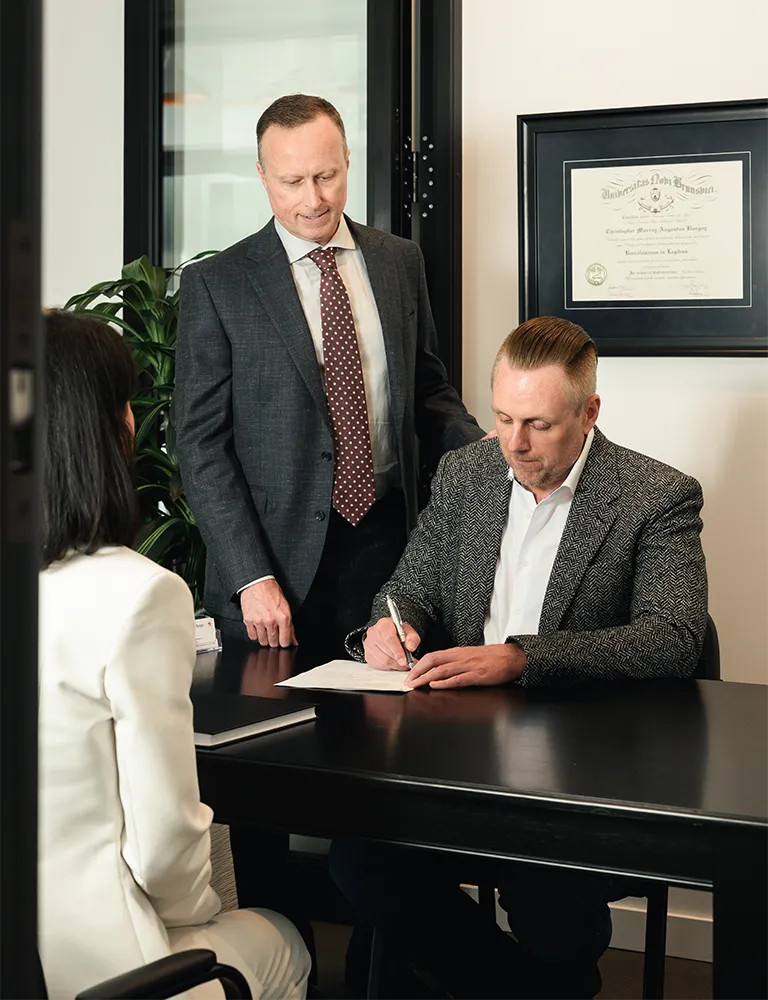 Business owner signing documents with Calgary family lawyer and his assistant